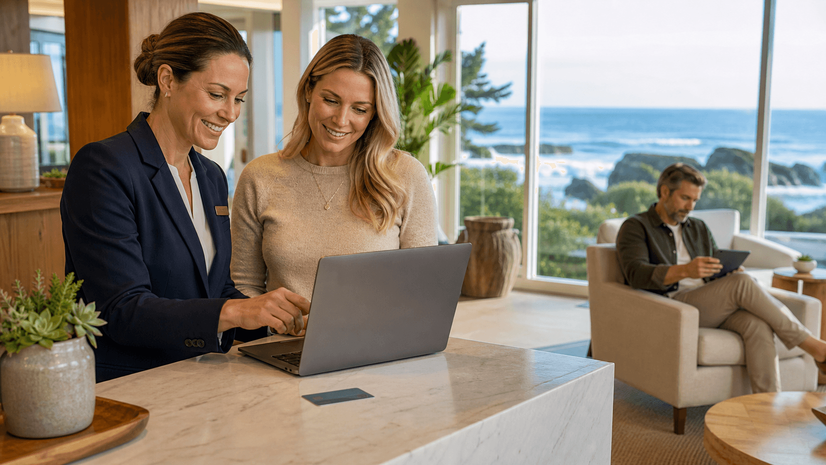 Laptop showing a booking calendar on a desk, with a coastal landscape and warm sunset colors in the background